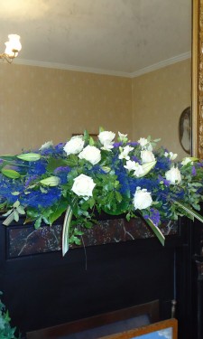 Mantelpiece arrangement with lily , rose, freesia, statice and blue sisal