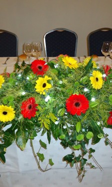 Top table arrangement of red and yellow gerbera, lily, solidago and lights