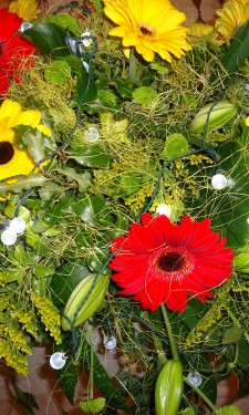 Top table arrangement of red and yellow gerbera, lily, solidago and lights