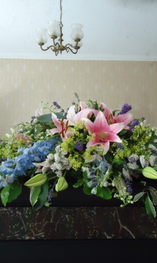 Mantelpiece arrangement with lily , delphinium, veronica, alchemilla mollis and lavendar