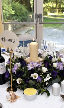 White & purple flowers in wreath ring with hurricane lamp, candle , sand and shells