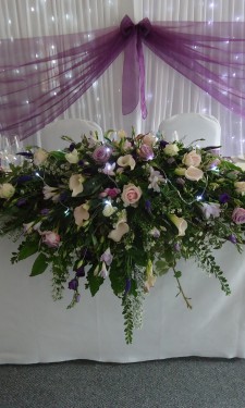 Top table arrangement containing roses, calla lilies, lizianthus, freesia, aster, mixed foliage and lights