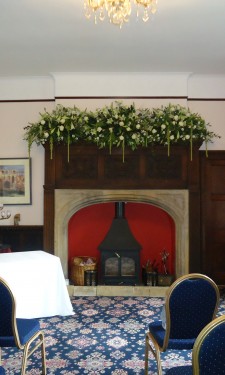 Mantelpiece arrangement with longiflorum lilies, roses, antirrhinums, trailing amaranthus and mixed foliage